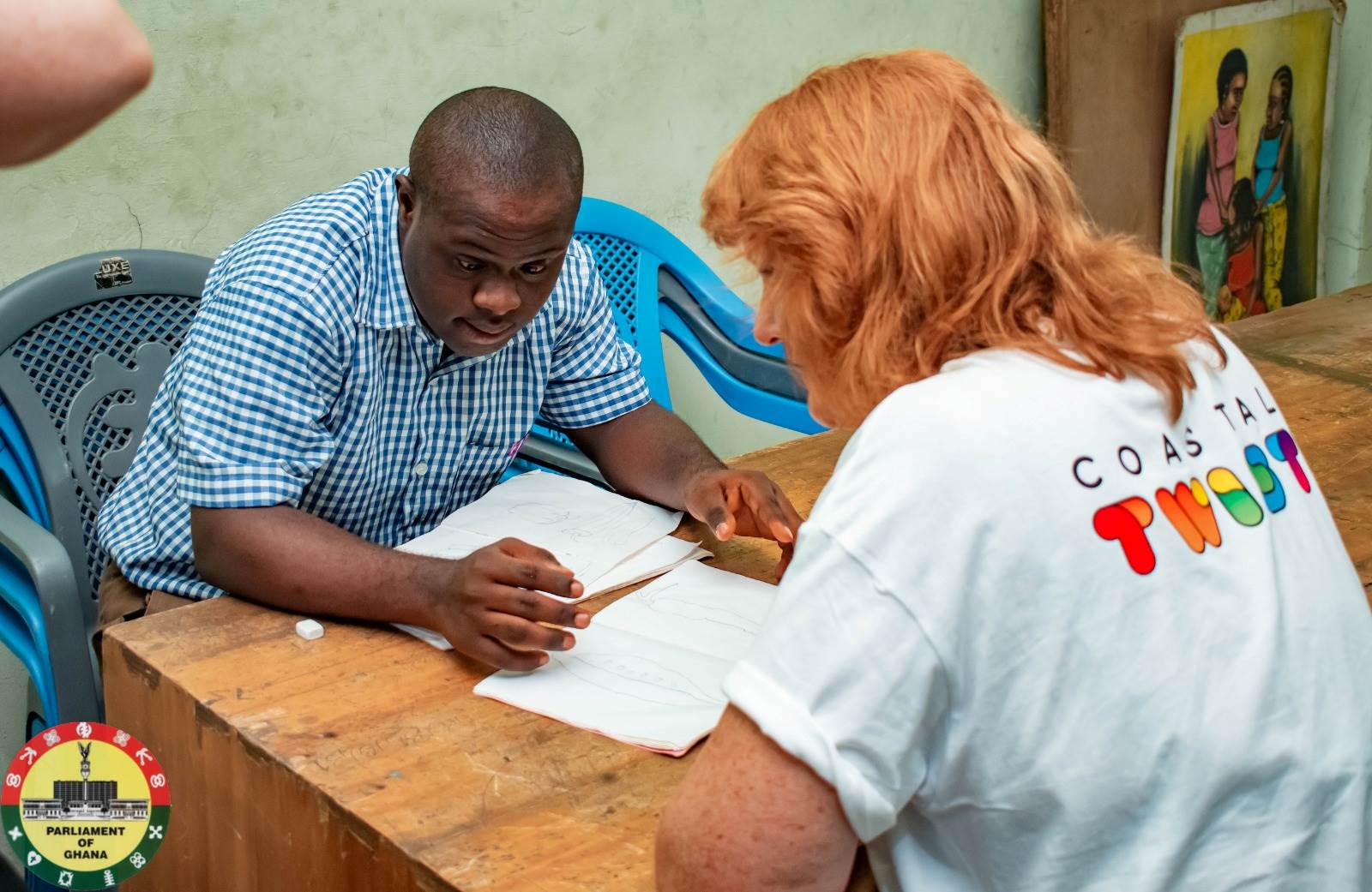 Liesl Tesch, a woman with ginger hair, sits with a young man wearing a checked blue shirt. They are both looking at documents on a table.